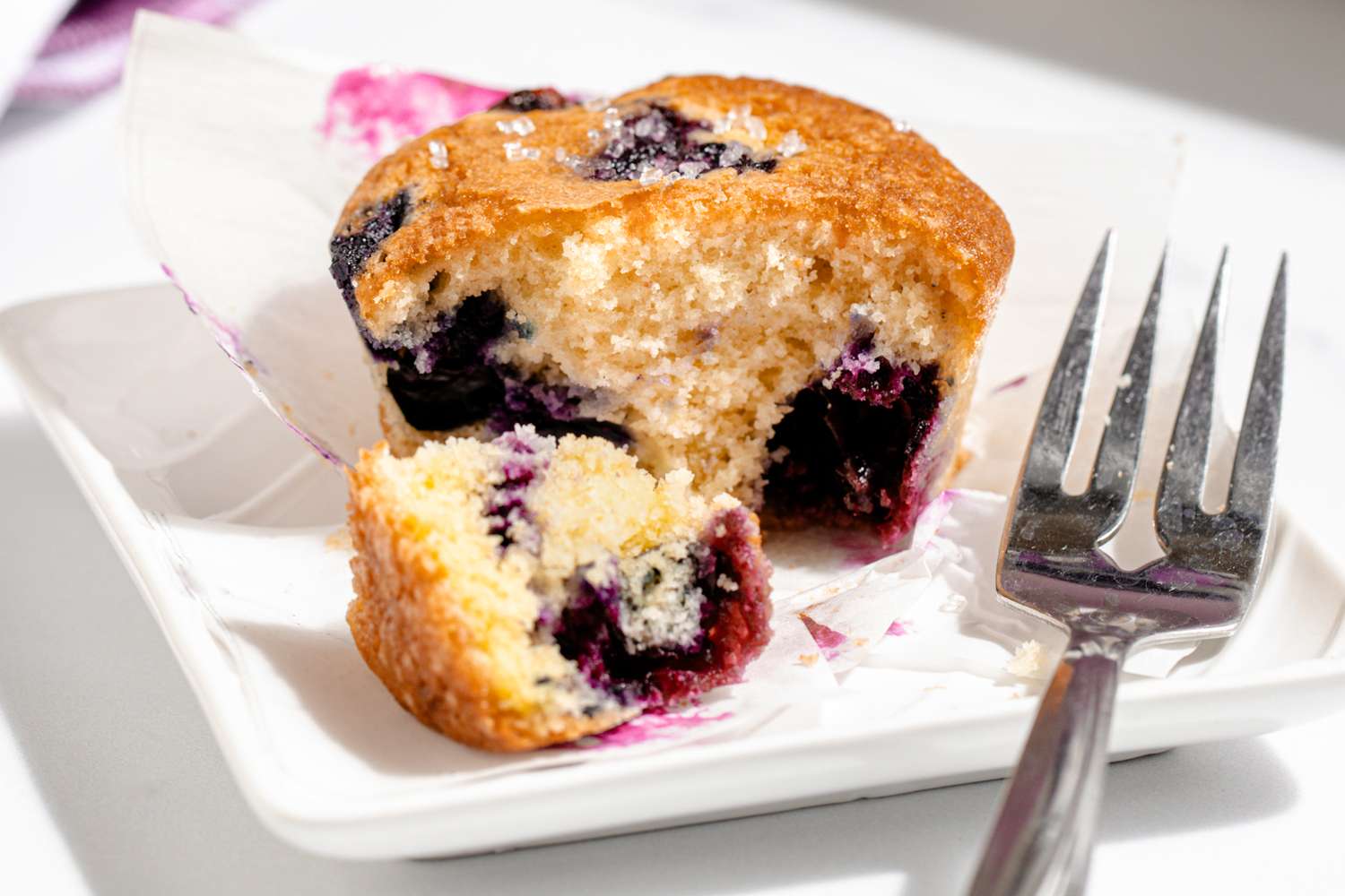 A blueberry muffin with a bite taken out on a plate with a fork beside it