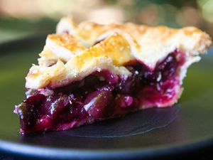 A slice of a cherry pie with a fresh cherry filling visible on the plate.
