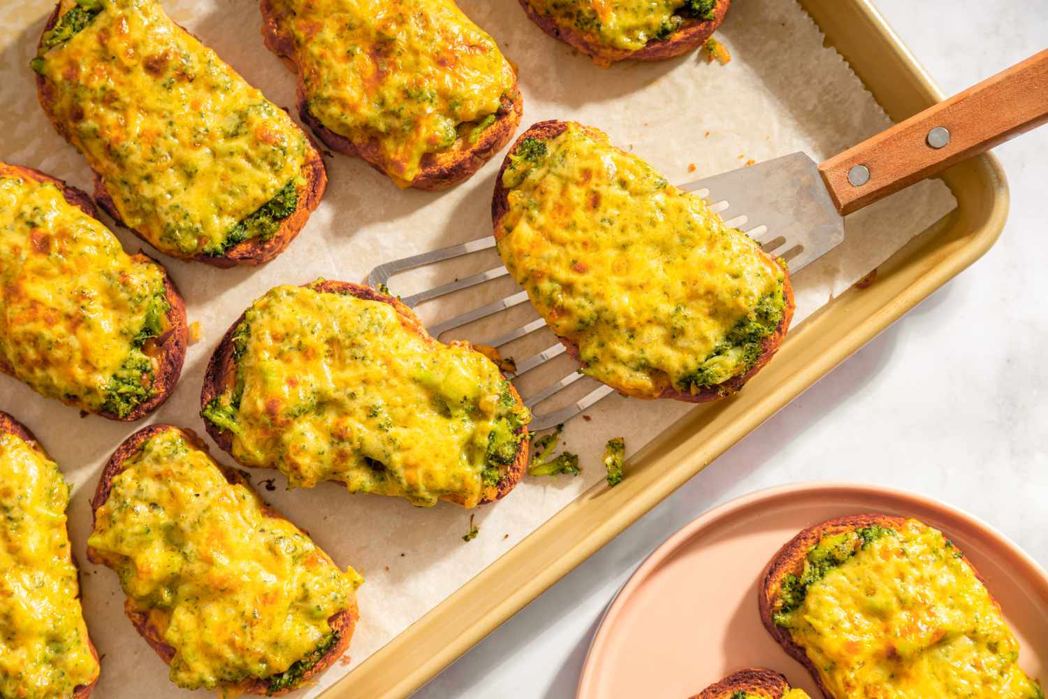 Broccoli cheddar toasts on a baking sheet a spatula lifting one