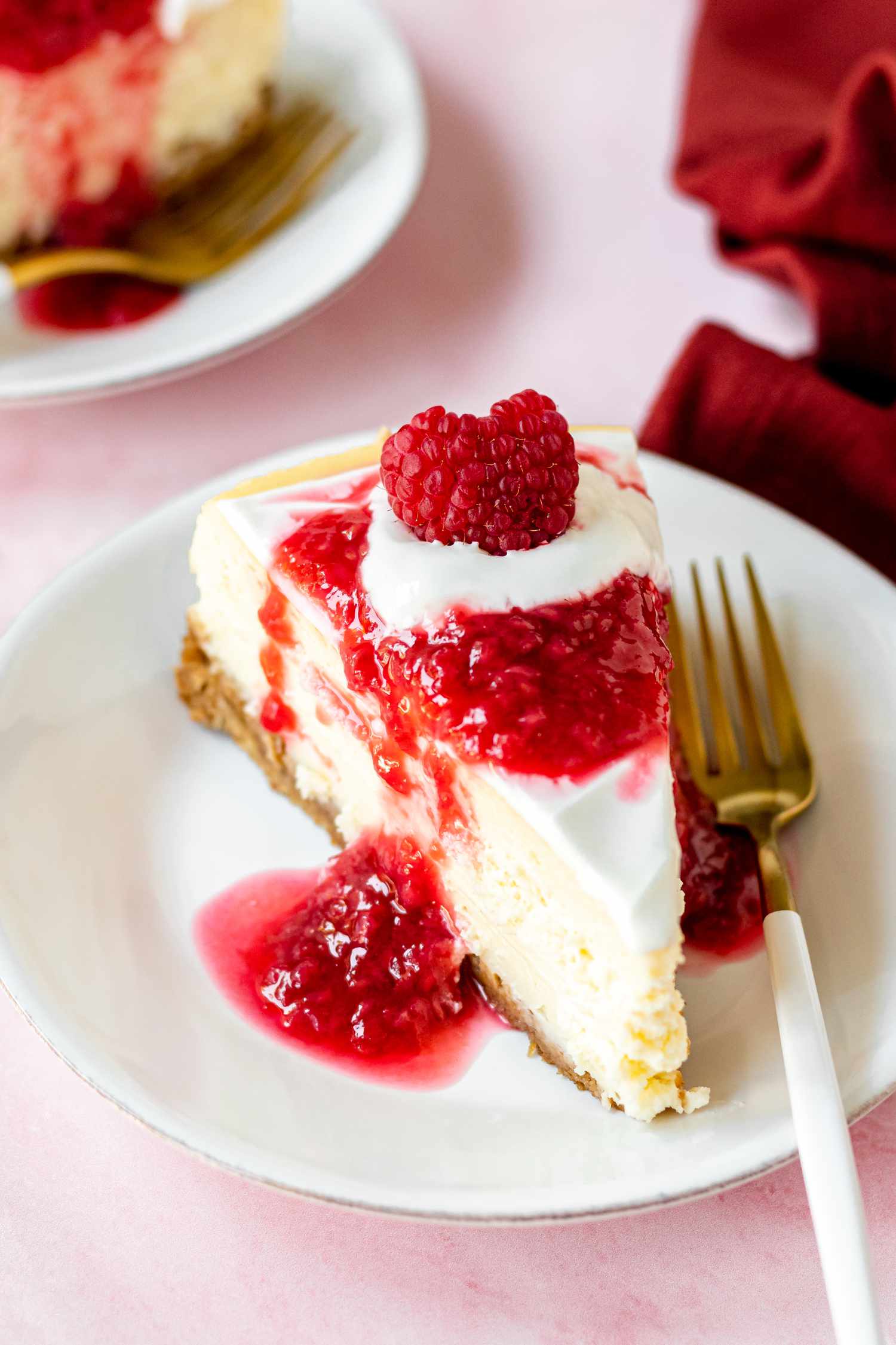 A slice of homemade cheesecake topped with raspberry sauce and on a plate with a fork.