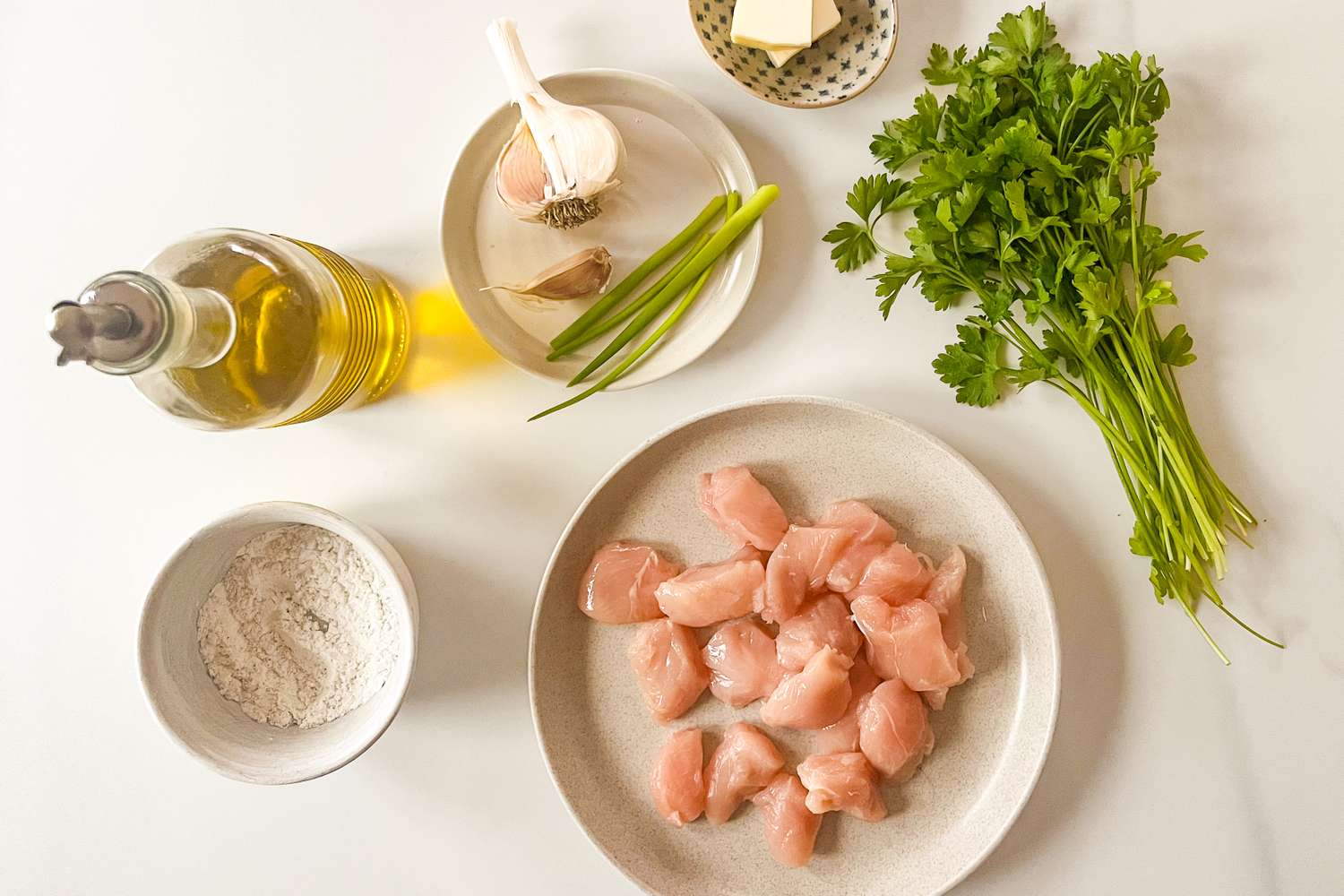 Ingredients for a chicken recipe arranged on a table including chicken pieces oil garlic parsley flour and butter