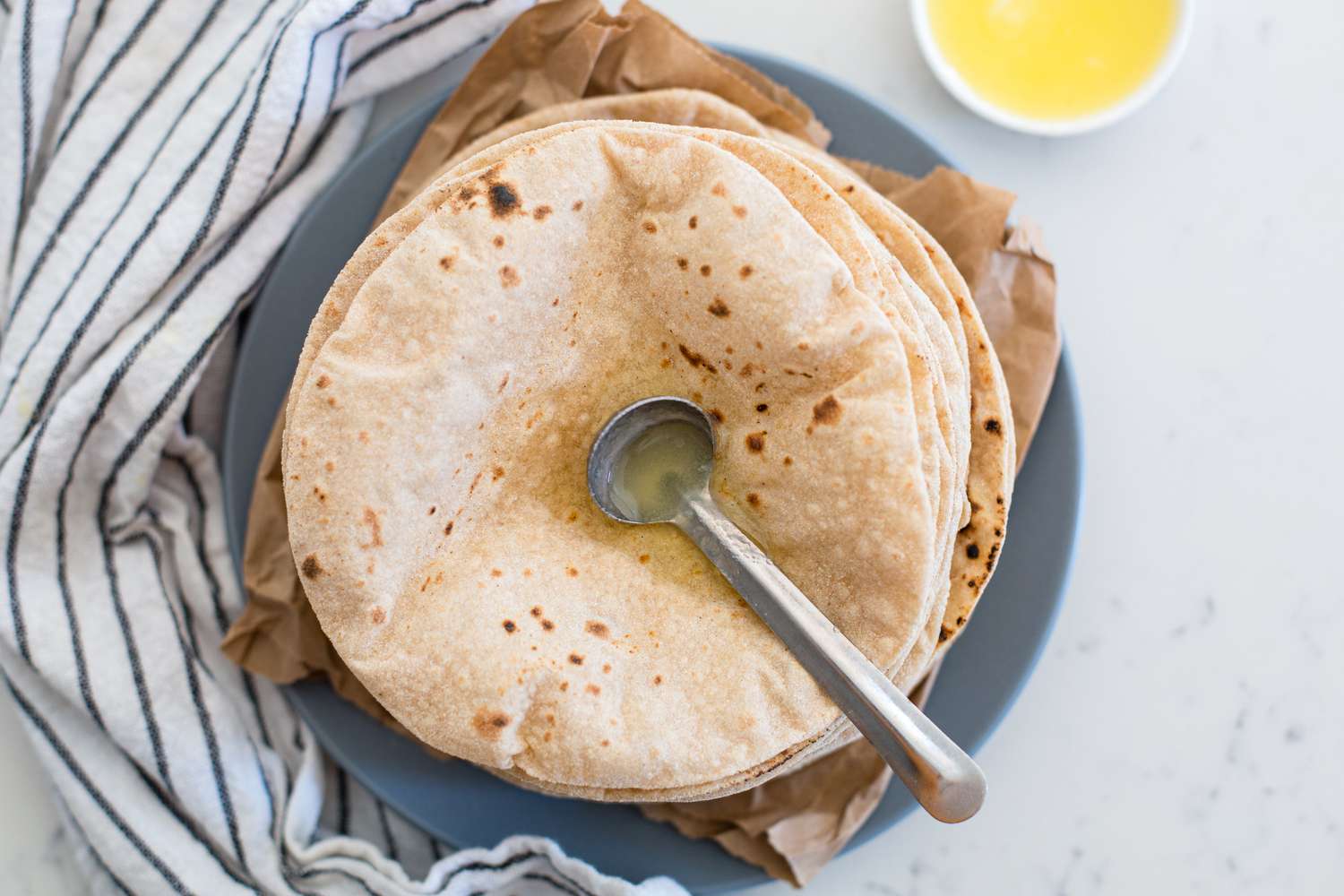 A stack of chapati with a small ladle of ghee on top.