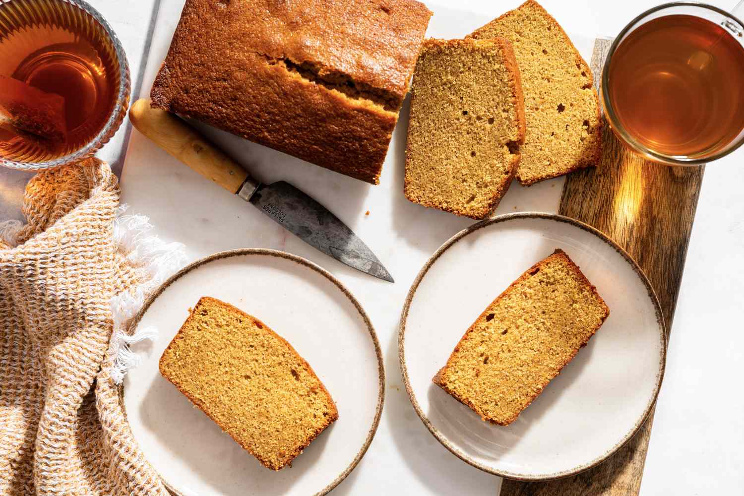 Sliced brown sugar pound cake served on plates with tea and a knife on the side