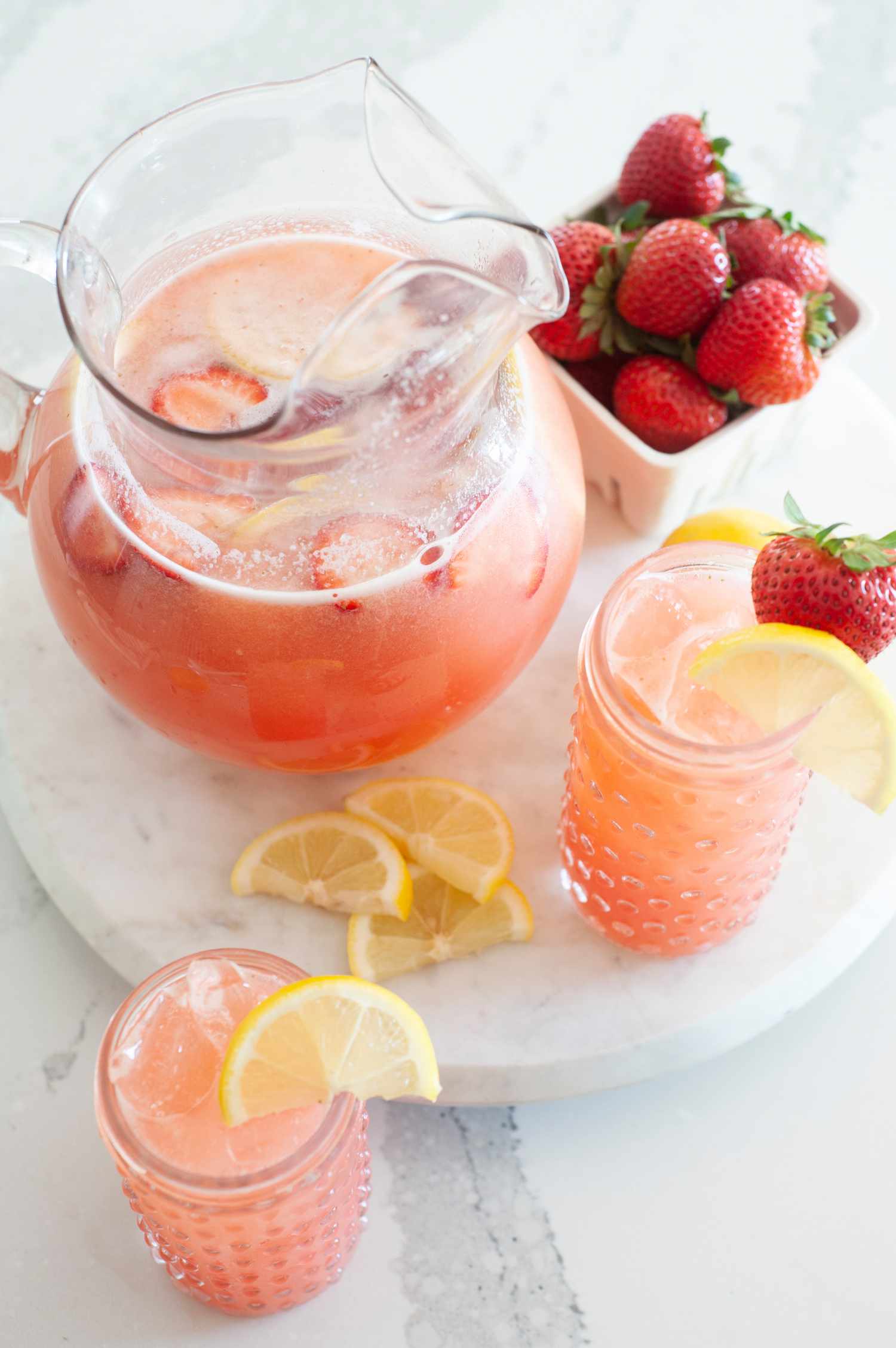 Overhead view of blender strawberry lemonade in a pitcher and two glasses and garnished with strawberry and lemon.