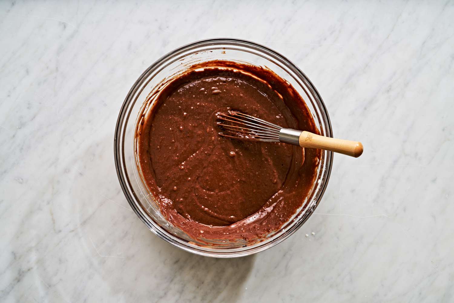 Overhead view of a clear glass bowl with a whisk after mixing the remaining ingredients to the coffee mixture for Mississippi Mud Cake recipe