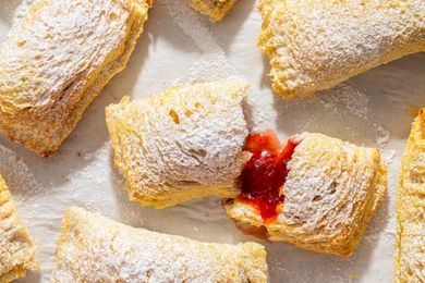 Toast Pies on a piece of parchment, dusted with powdered sugar, one torn open to show red filling