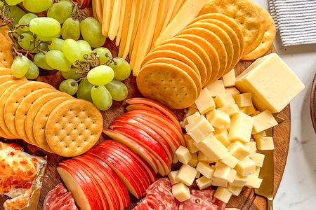An arrangement of fruit cheese crackers and deli meats on a wooden board