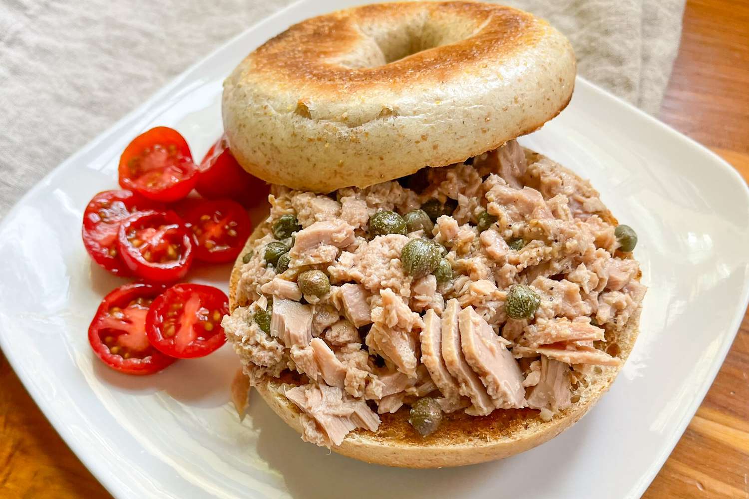 3-ingredient tuna salad on a toasted bagel on a plate with a serving of halved grape tomatoes