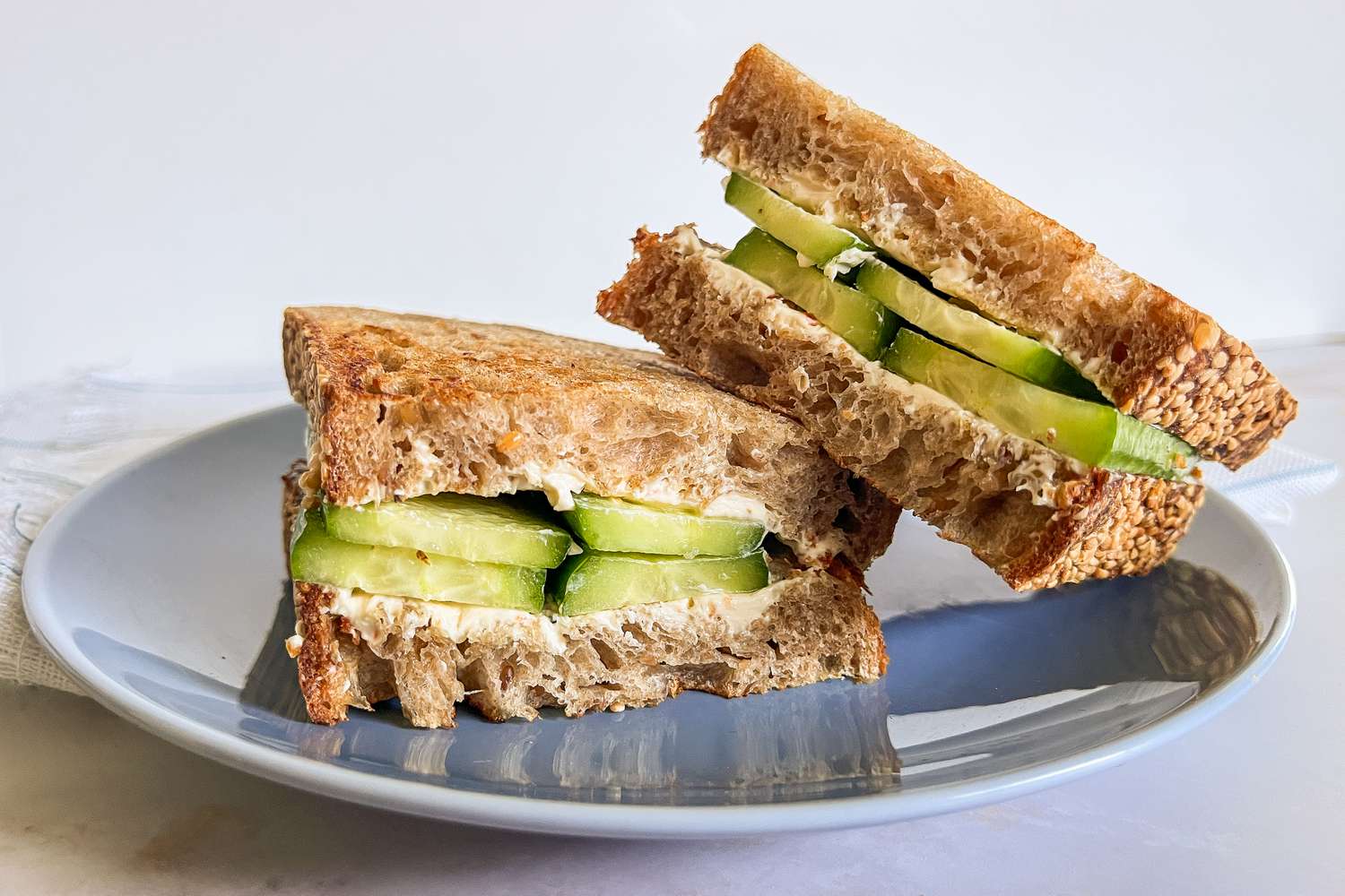 Halved 2-ingredient cucumber sandwich on a plate, with one sandwhich half leaned on another 