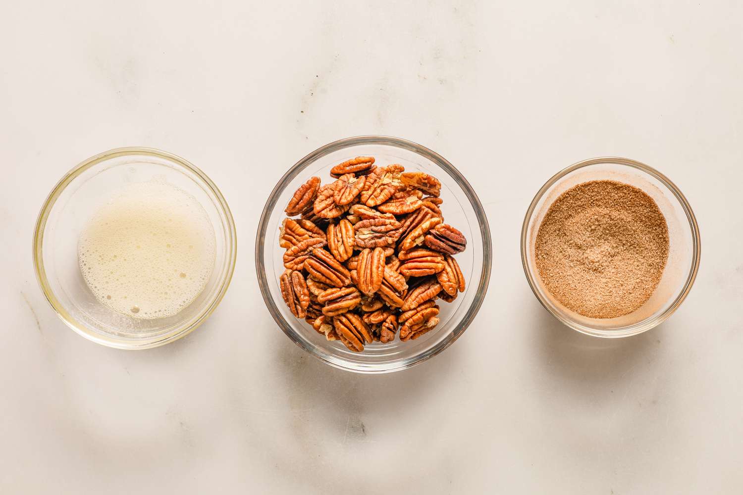 Overhead view of three small glass bowls with pecans, cinnamon sugar mixture and egg whites ready for topping cookies from Sand Tarts recipe