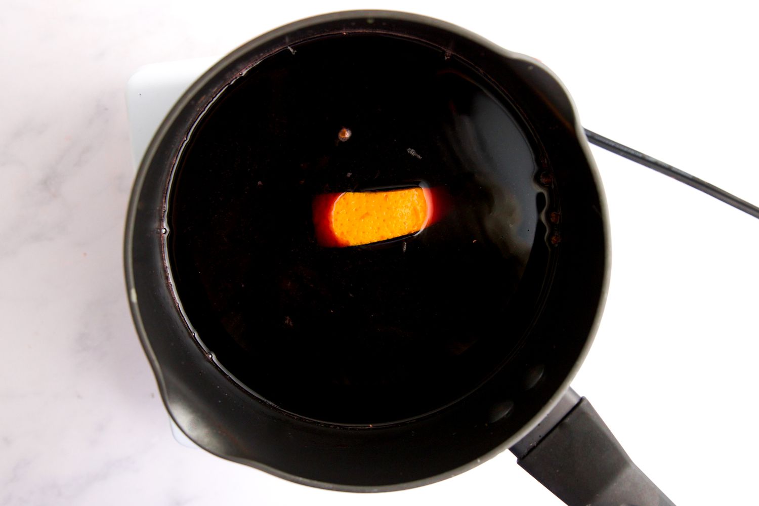 Red wine sauce with orange peel in pot.