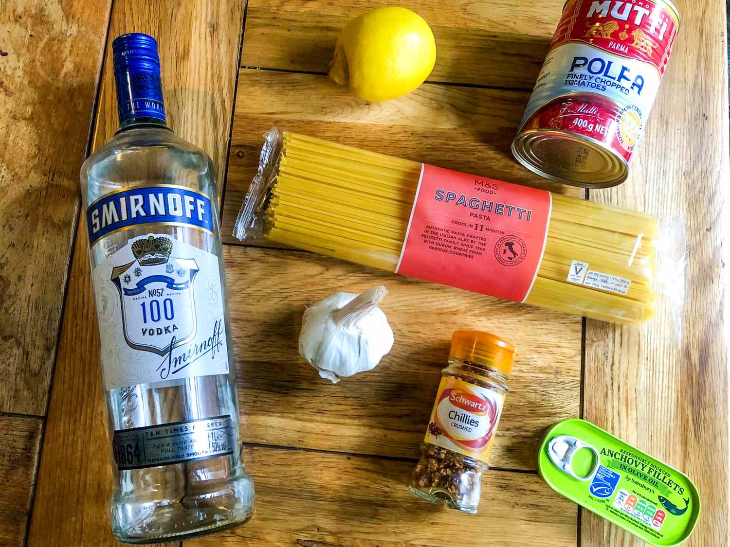 A selection of ingredients for cooking on a wooden table vodka lemon pasta canned tomatoes garlic red pepper flakes and anchovy paste