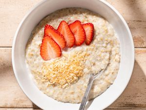 Coconut oatmeal topped with sliced strawberries and toasted coconut, served in a bowl with a spoon.