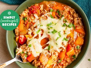 A bowl of hearty soup topped with melted cheese and parsley featuring meat vegetables and rice