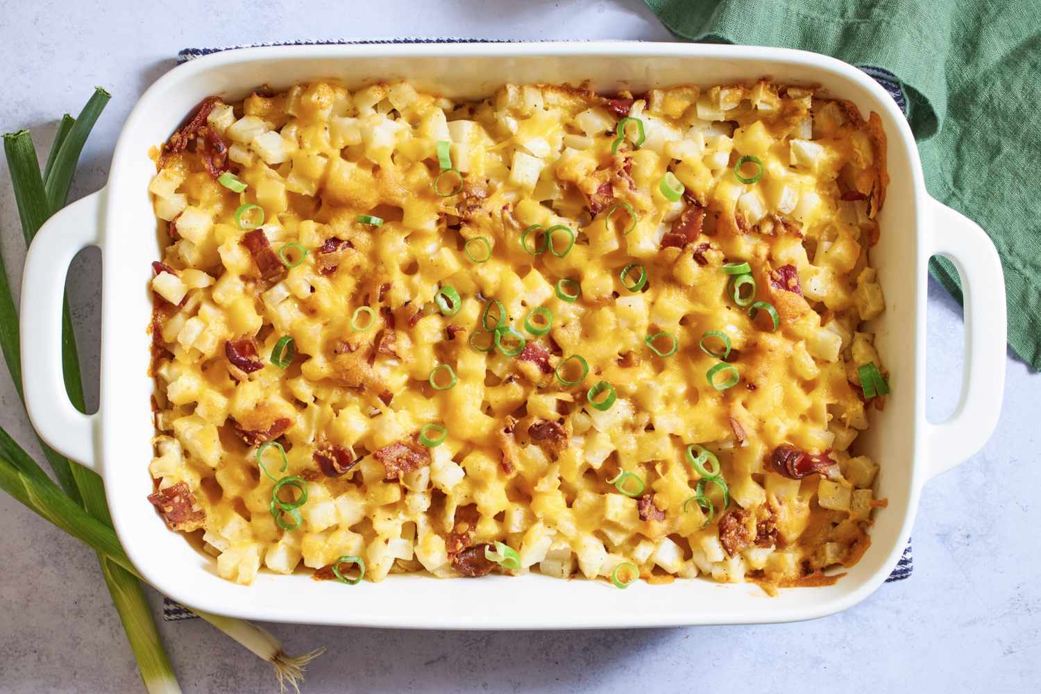 Baked casserole with diced ingredients melted cheese and garnished with green onions in a rectangular dish