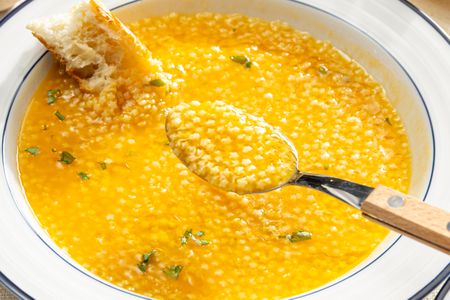 A bowl of pastina in brodo with a spoon and a piece of crusty bread