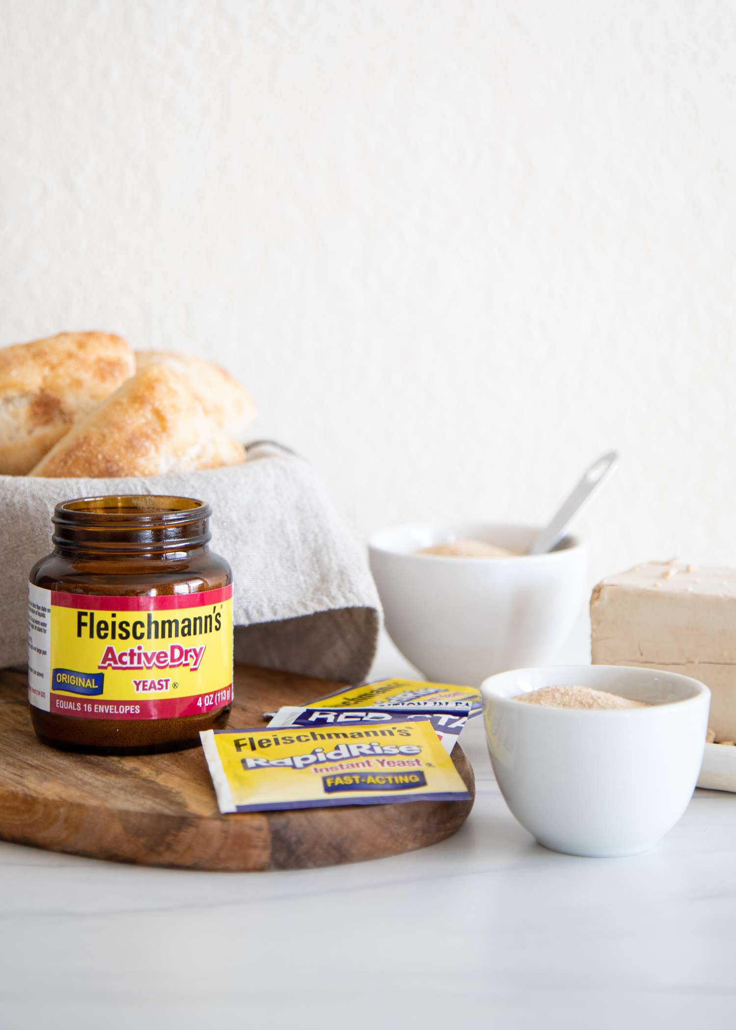Side view of different types of yeast and a bowl with bread behind them.