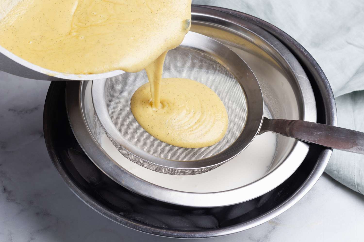 Straining the custard into a strainer set over a bowl of cream for a homemade ice cream recipe.