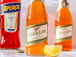 Miller High Life beer bottle with a lemon wedge Aperol bottle in the background