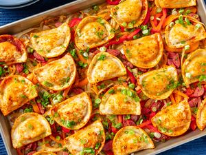 A tray of baked pierogis garnished with green onions layered over sauted vegetables