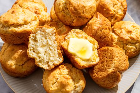 Mayonnaise Muffins on a platter, one muffin on top is cut in half, one side spread with butter