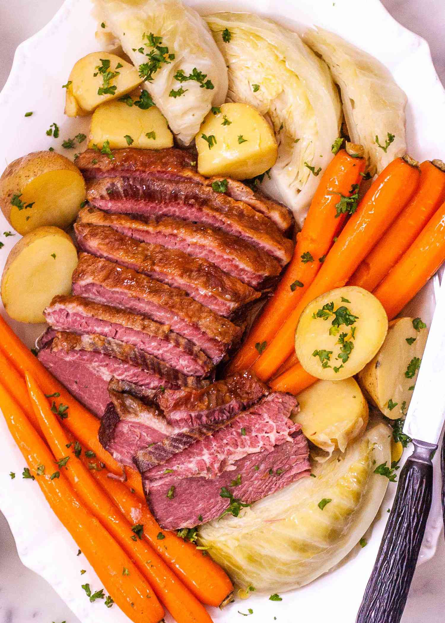 How to Boil Corned Beef and Cabbage - platter of sliced corned beef, carrots, potatoes, and cabbage sprinkled with herbs
