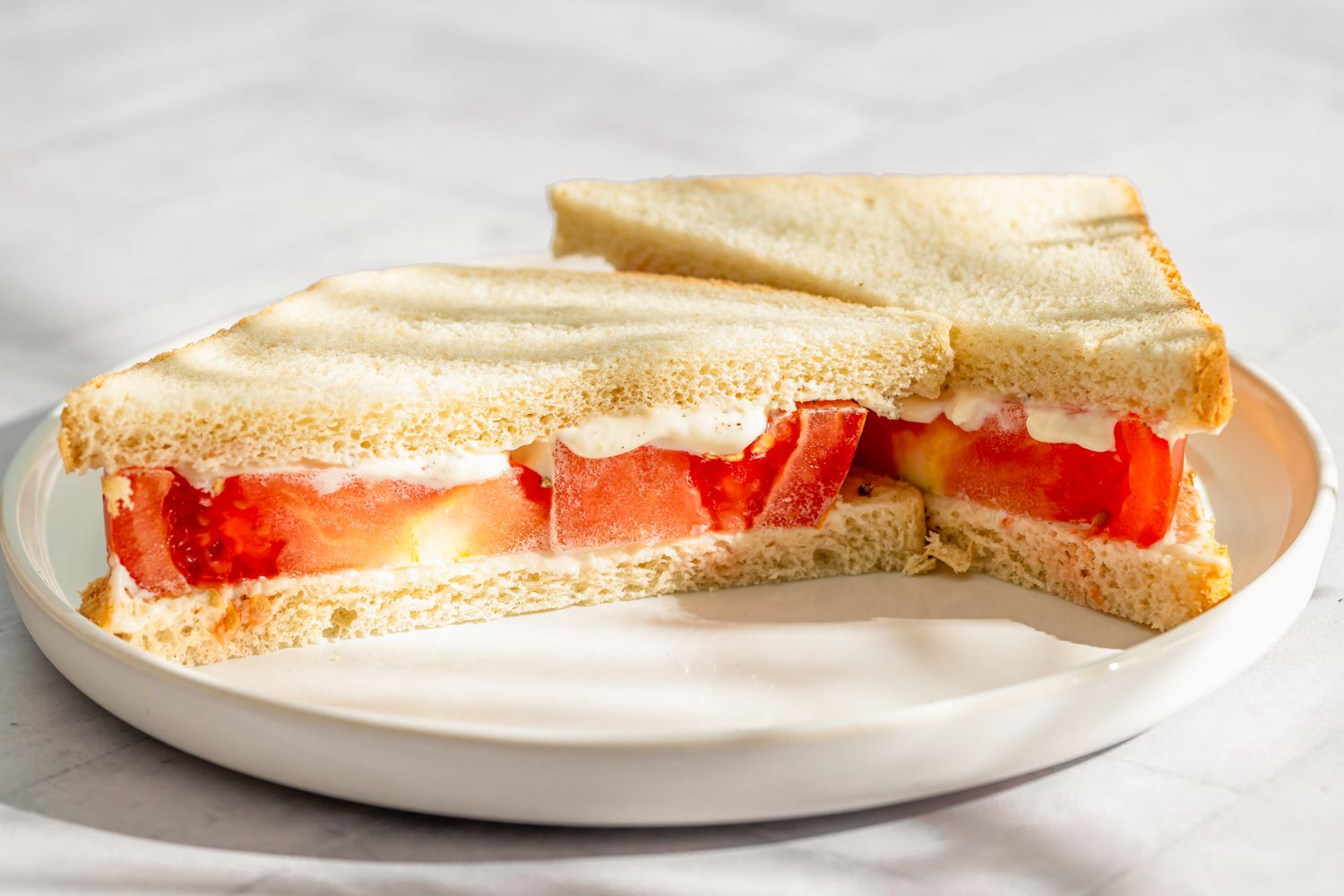 Tomato sandwich on white bread cut diagonally on a white plate