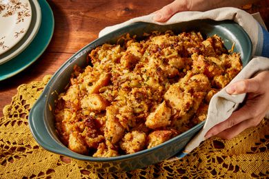 Two hands holding a green casserole dish of Wisconsin-style stuffing over a yellow doily on a wooden tabletop