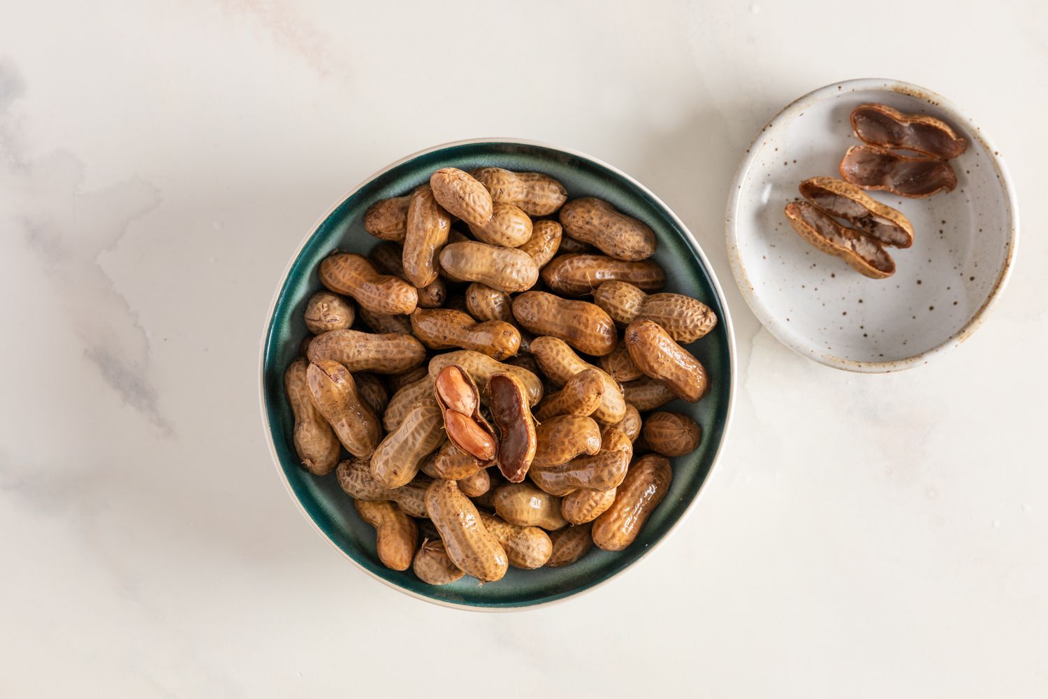 A bowl of boiled peanuts on a table with shelled boiled peanuts in the background