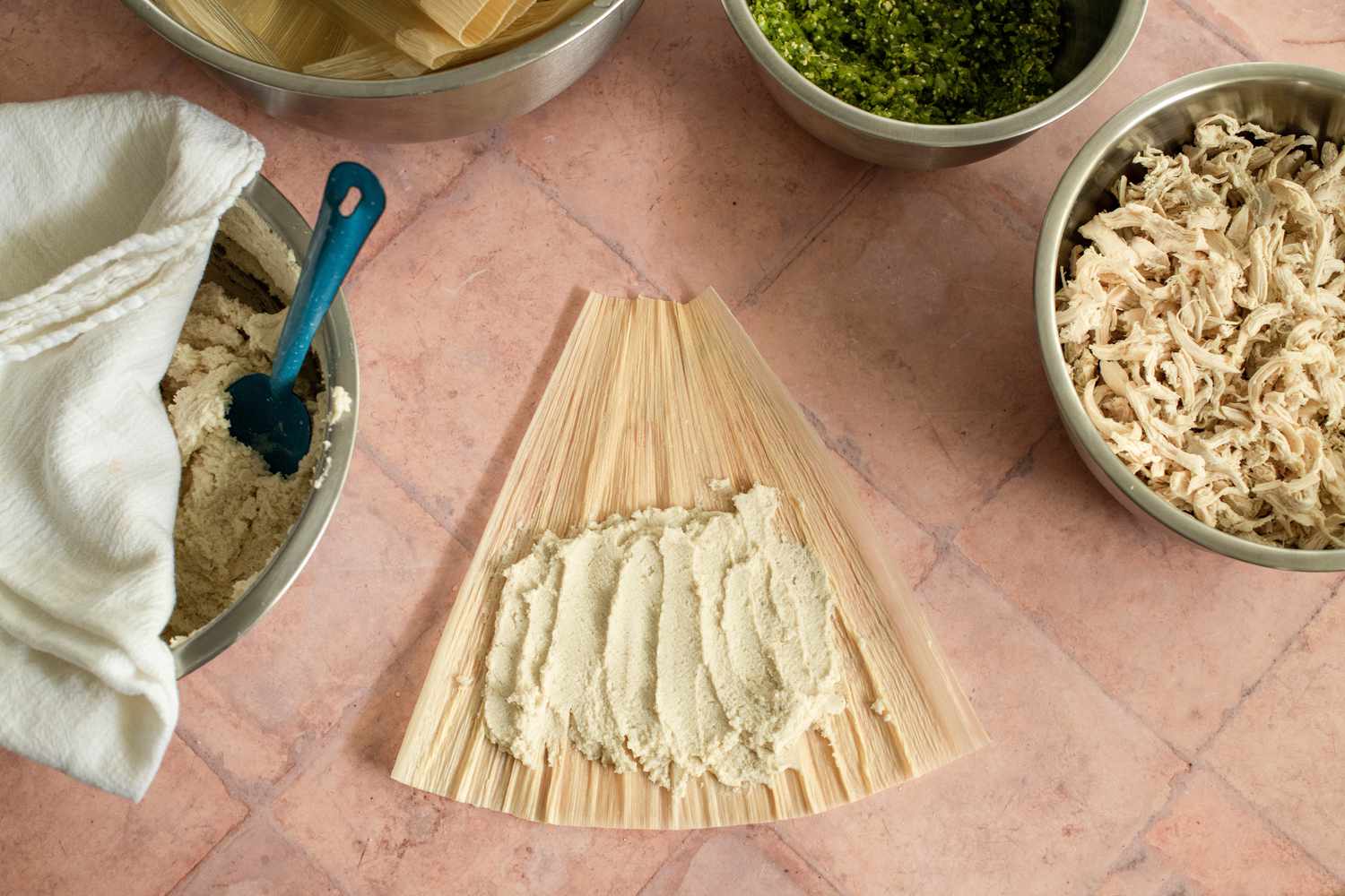 Masa Spread on a Corn Husk and in the Surrounding, Bowls of Ingredients (Masa, Corn Husks, Chile Verde, and Shredded Chicken)