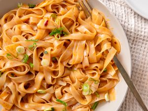 Overhead closeup shot of a serving plate with broad rice noodles in a garlic sauce, garnished with sliced scallions