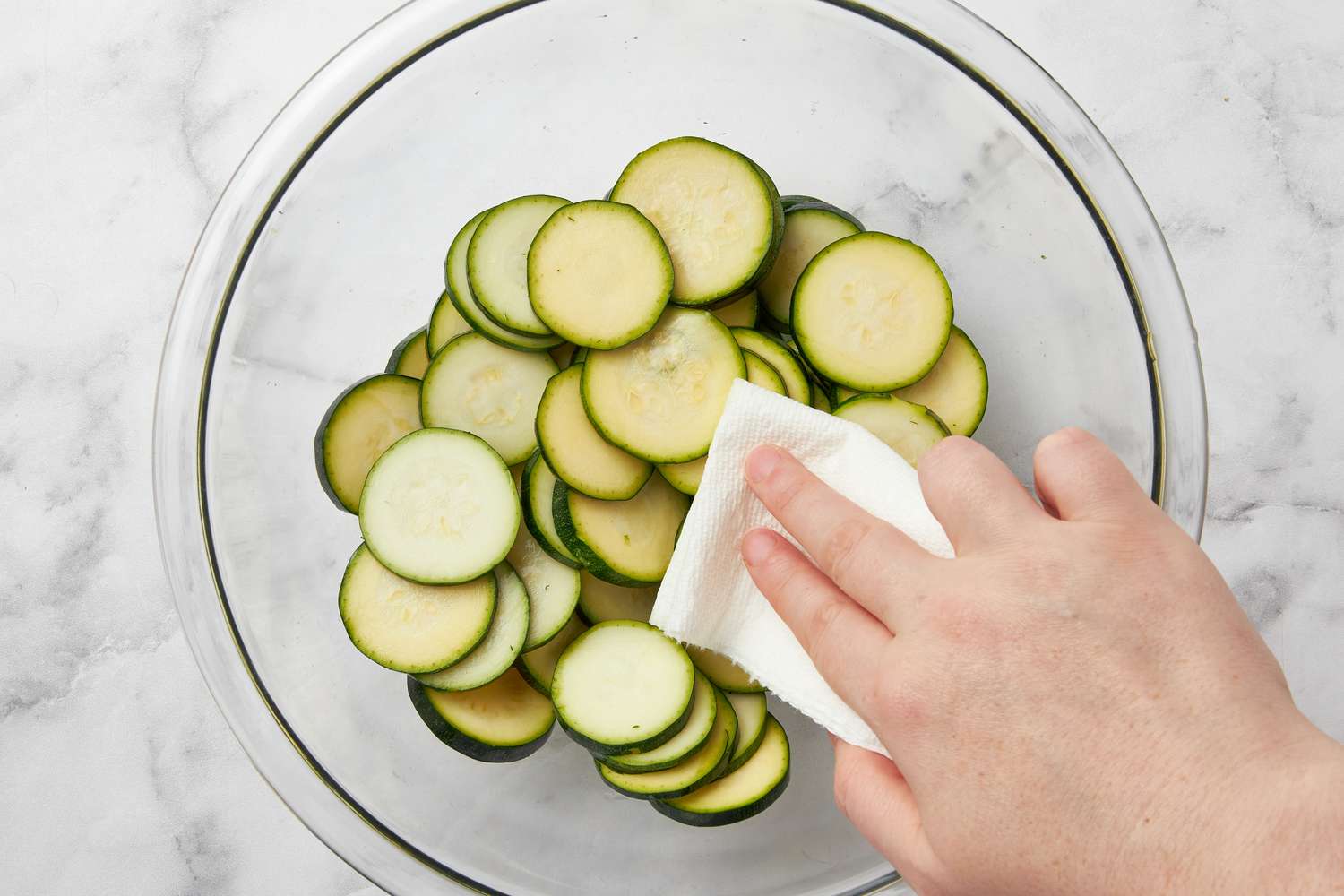 Patting zucchini slices dry with a paper towel