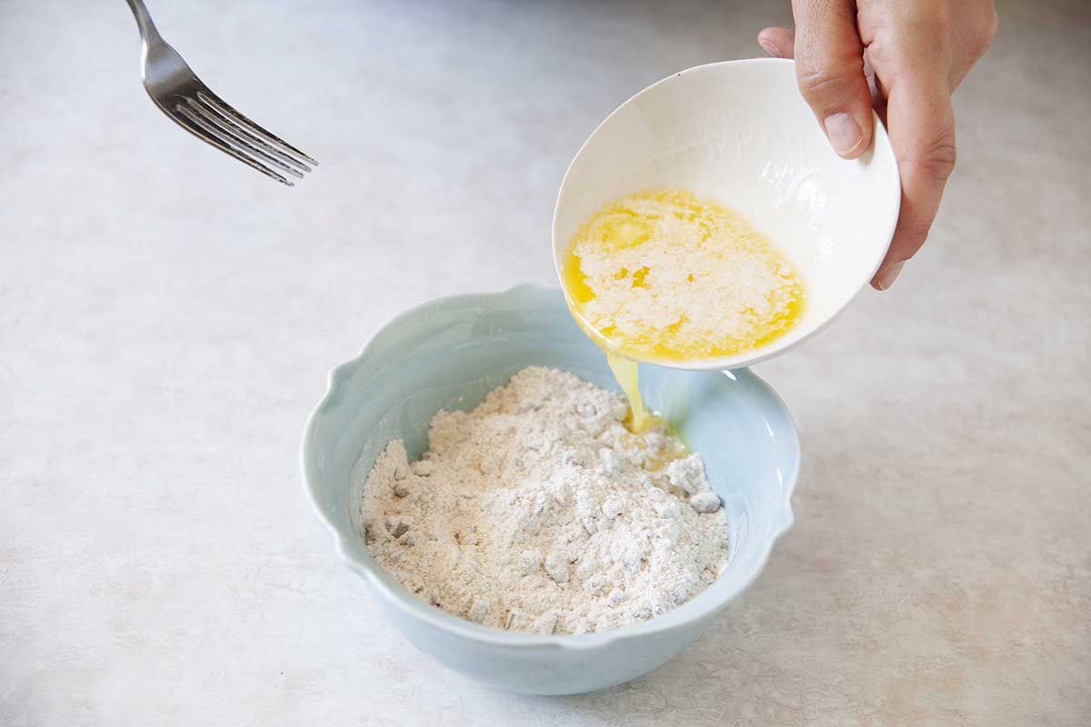Woman pouring butter into a blue bowl filled with crumble topping.