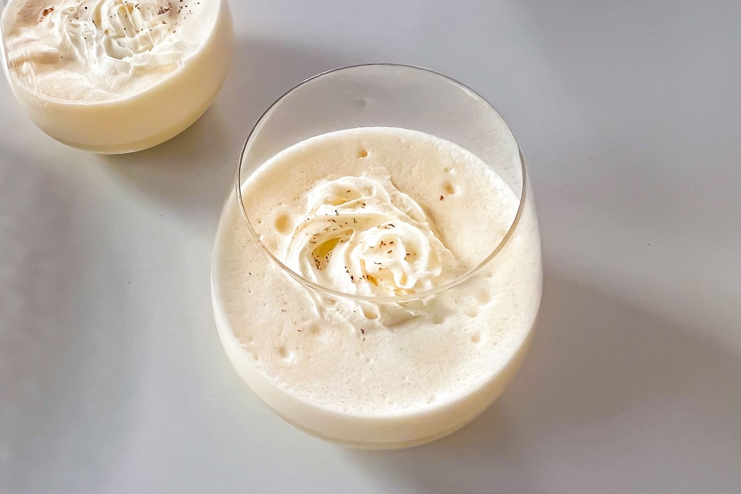 Two glasses of eggnog topped with whipped cream