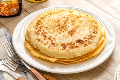 Plate of Pannenkoeken (Dutch Pancakes) on a plate next to a stripped kitchen towel with forks and a container of syrup