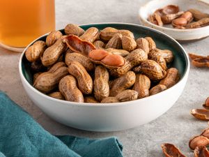 A bowl of boiled peanuts on a table with shelled boiled peanuts in the background