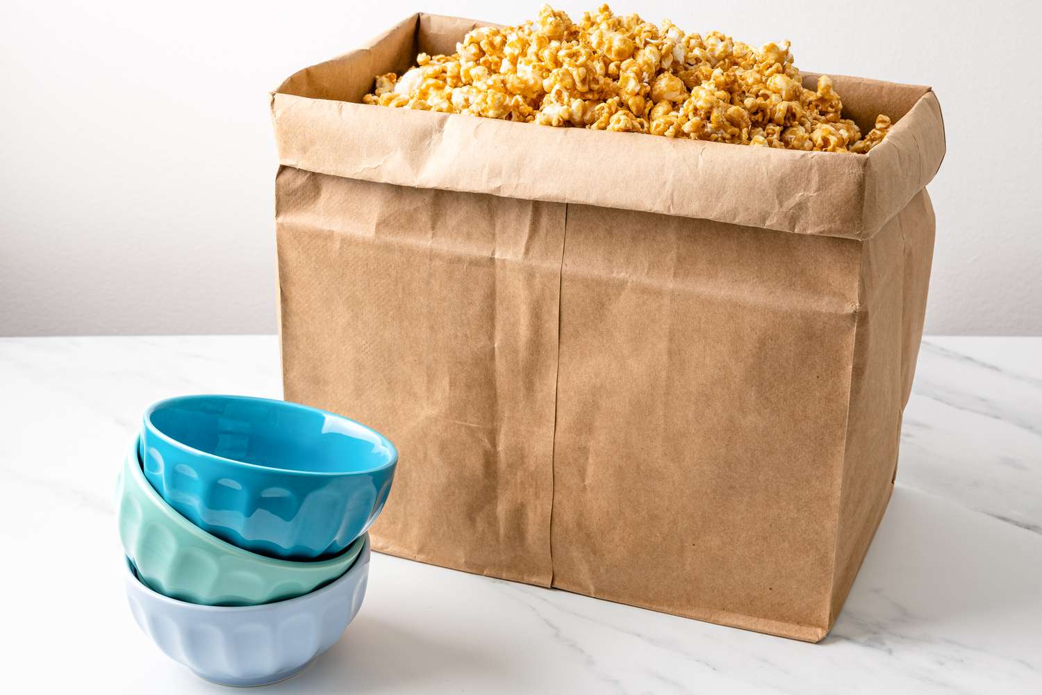 caramel corn in a paper bag with colorful bowls next to it