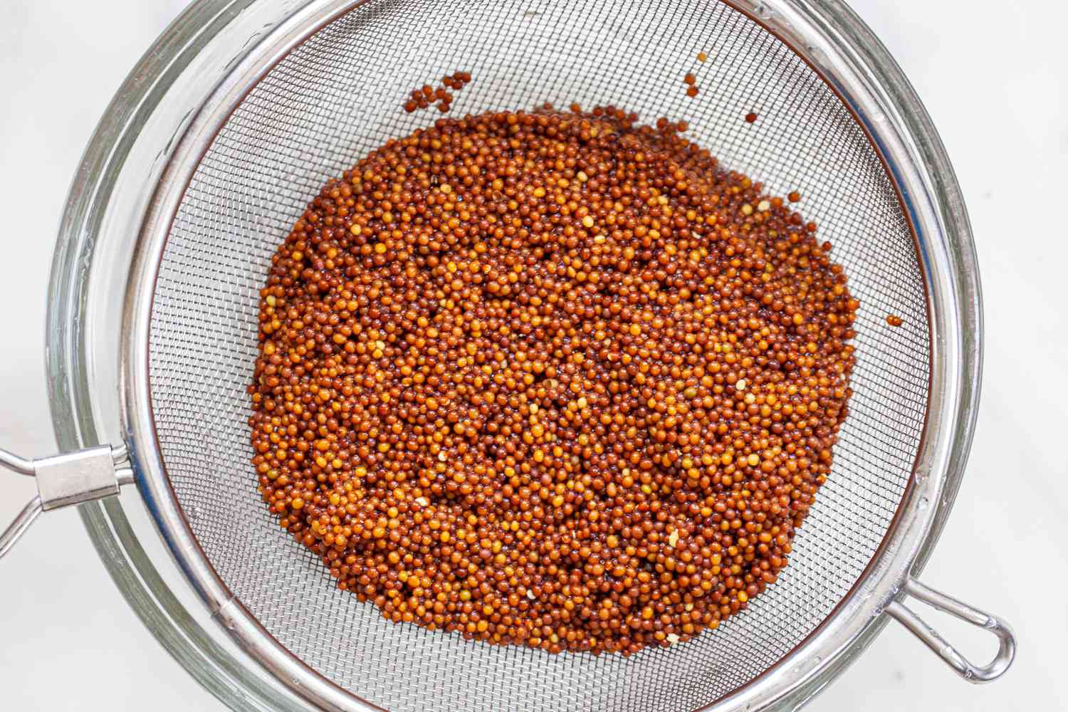 Straining mustard seeds to make Dijon mustard from scratch.
