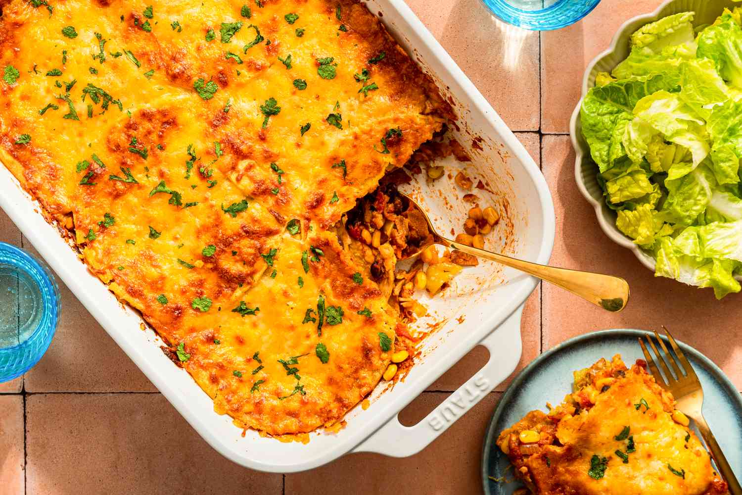 Chicken taco casserole (with a serving cut out) at a table setting with a serving on a plate, glasses, and a side salad