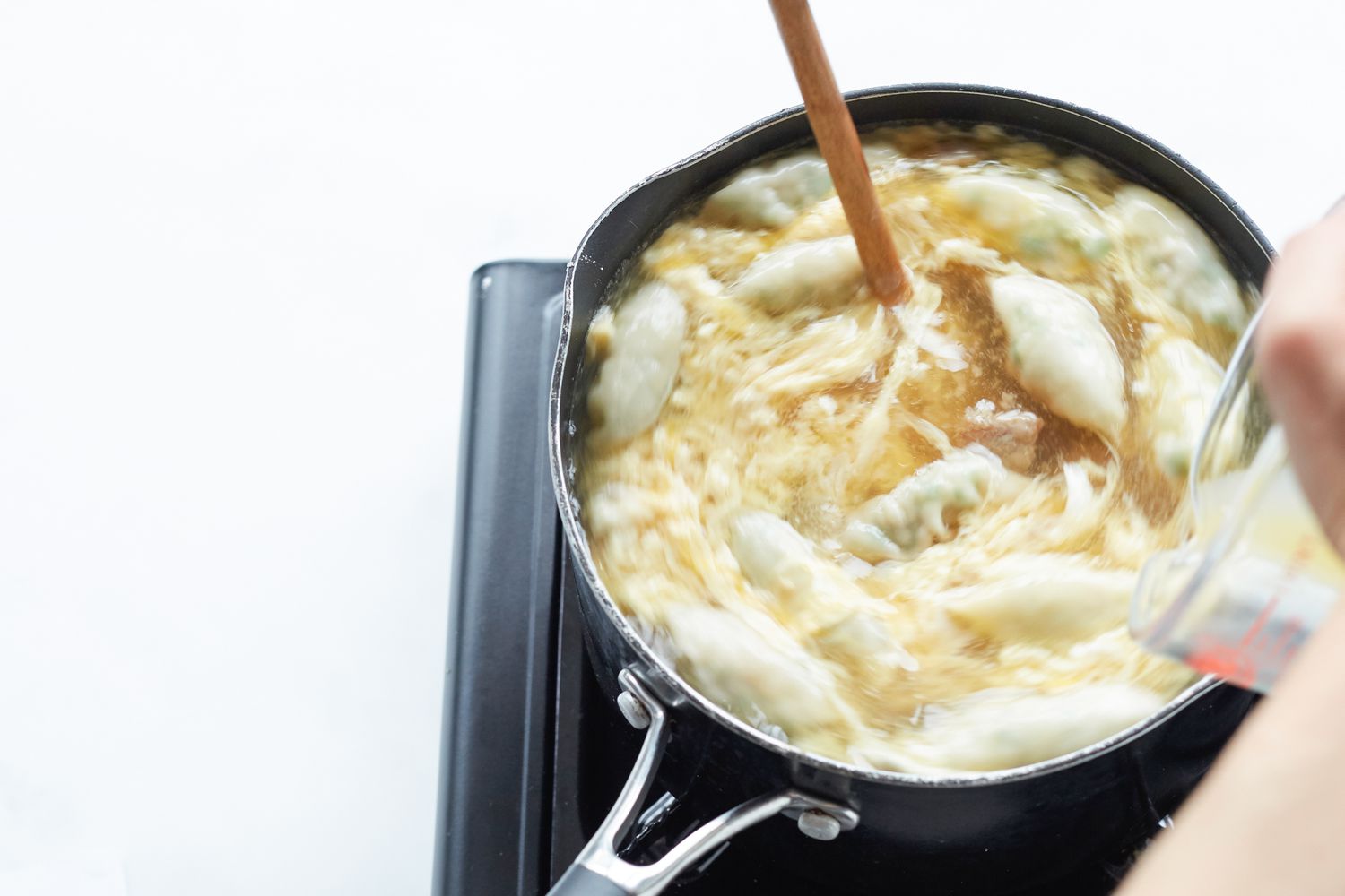 Drizzling in whisked eggs to a Korean dumpling beef soup in a pot on the stove.