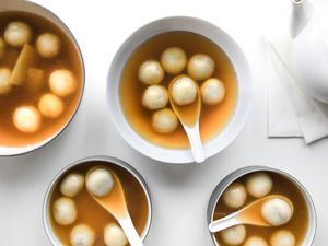 Three Bowls of Red Bean Tangyuan with Soup Spoons, and on the Left, a Pot with More and on the Right, a Tea Kettle Sitting on Napkins