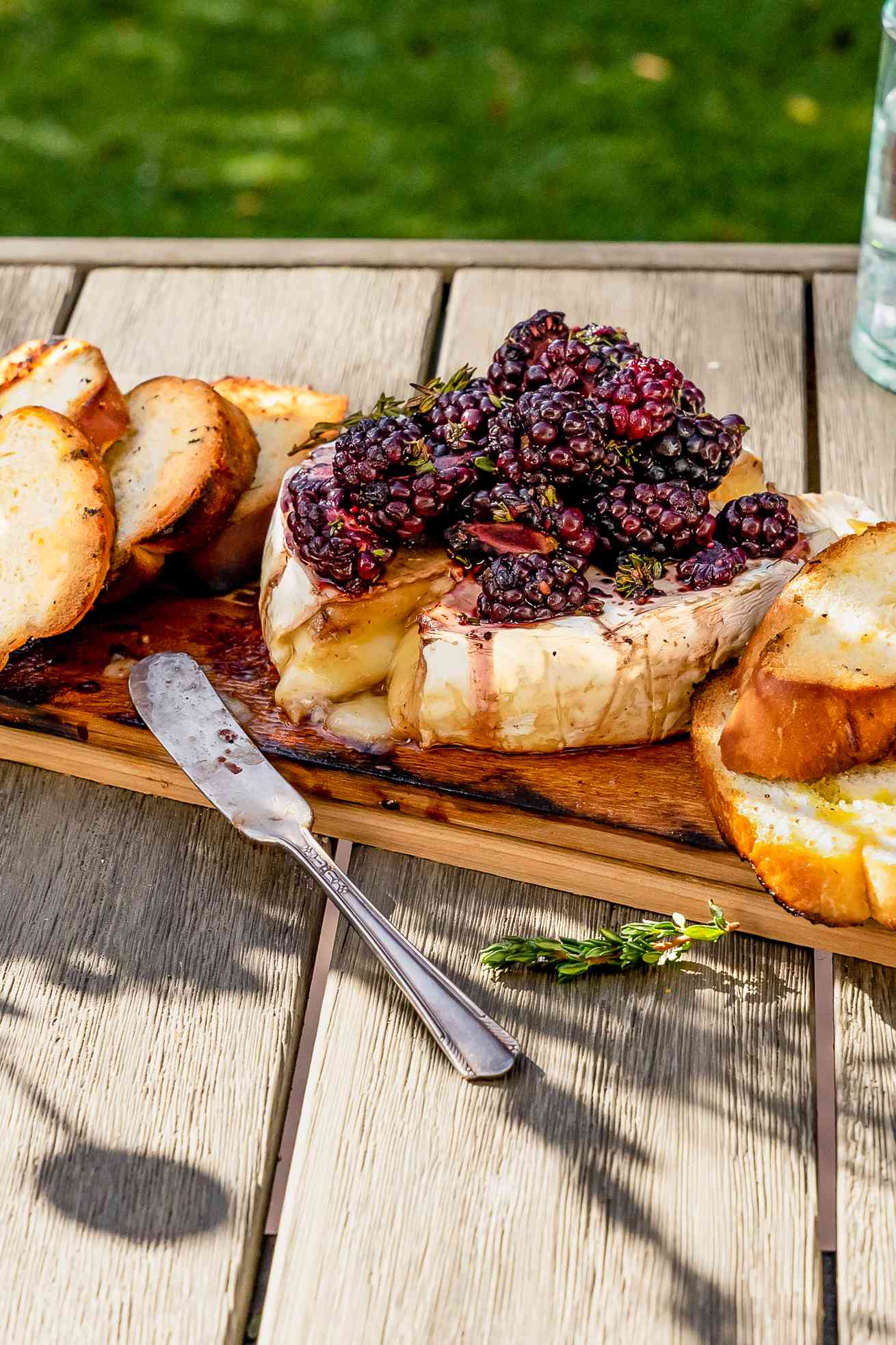 Cedar Plank Grilled Brie Topped With Black Berries and a Sprig of Thyme, and on the Plank Next to the Brie, Slices of Baguette