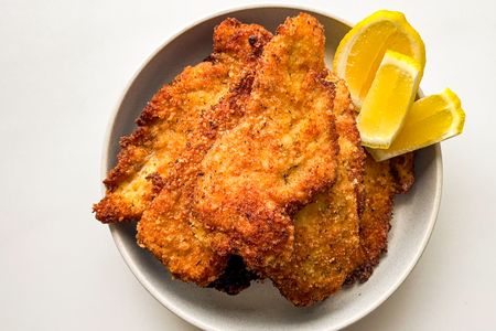 Breaded chicken cutlets served on a plate with lemon wedges