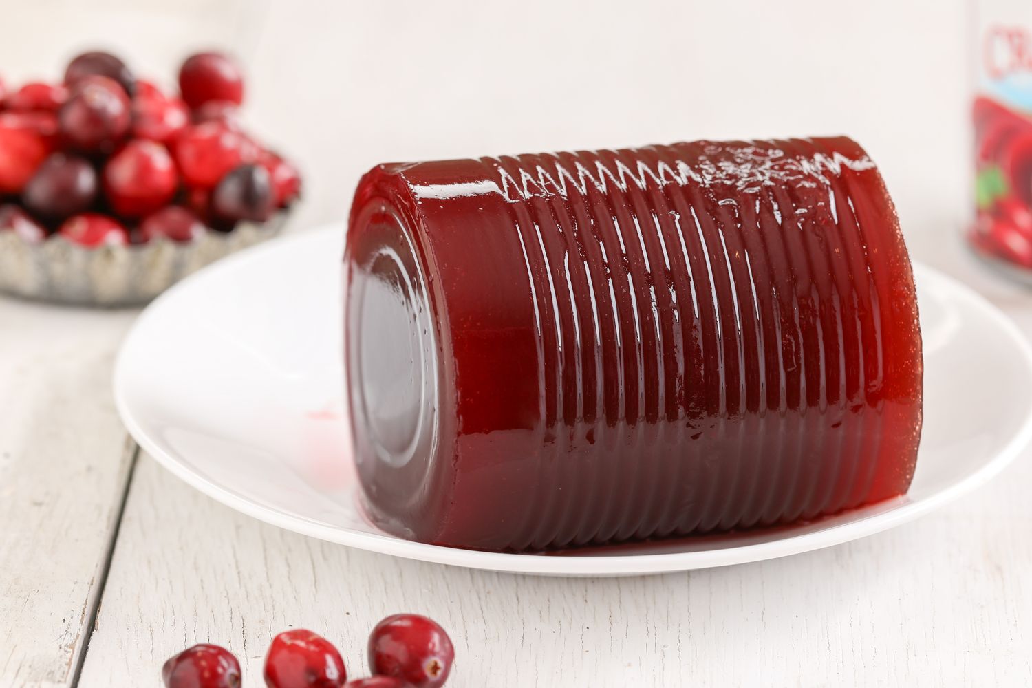 A dish with a cylindrical block of gelatinized cranberry sauce surrounded by scattered fresh cranberries
