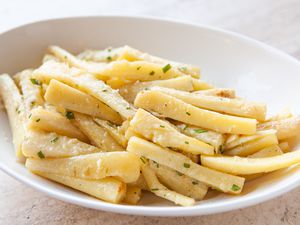 A white serving dish with roast parsnips inside.