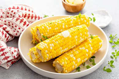 Several ears of corn on the cob in a serving dish with a pat of butter melting on top