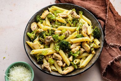 Bowl of Chicken and Broccoli Pasta Next to a Kitchen Towel and a Small Bowl of Cheese