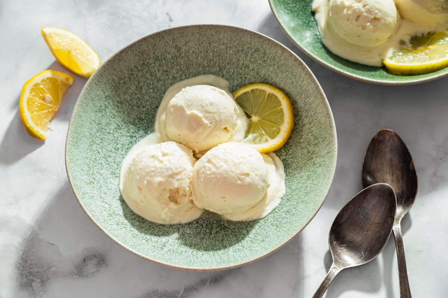 Three scoops of sorbet in a bowl garnished with a lemon slice with two spoons nearby