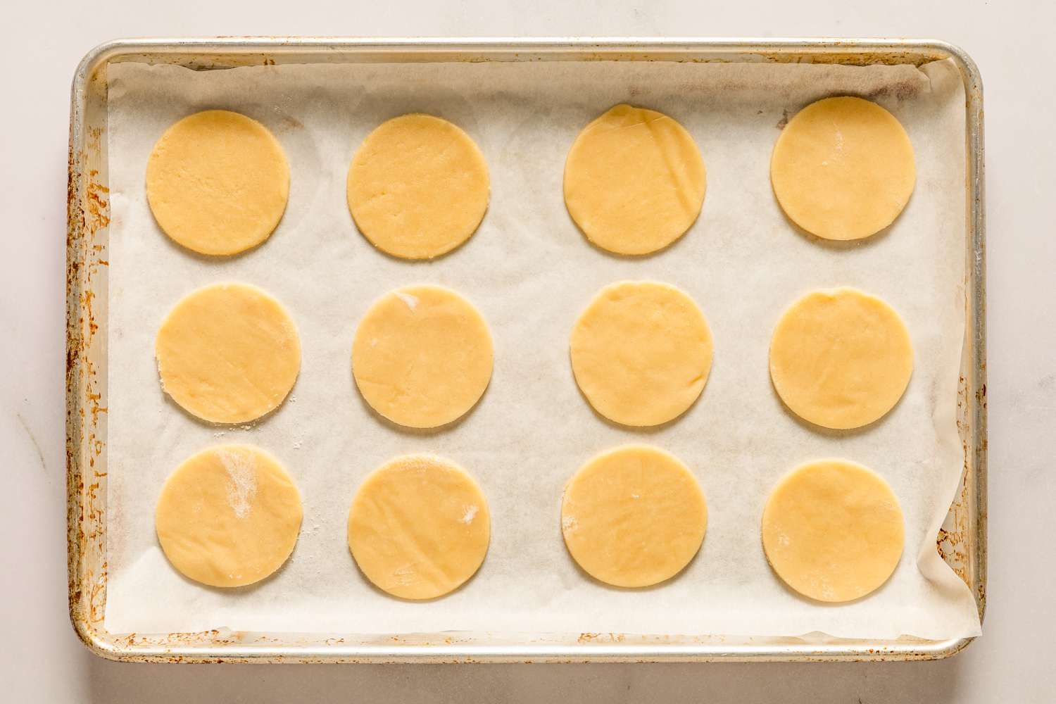 Overhead view of a metal baking sheet lined with parchment paper and with twelve cookies cut out with round cookie cutter for Sand Tarts recipe