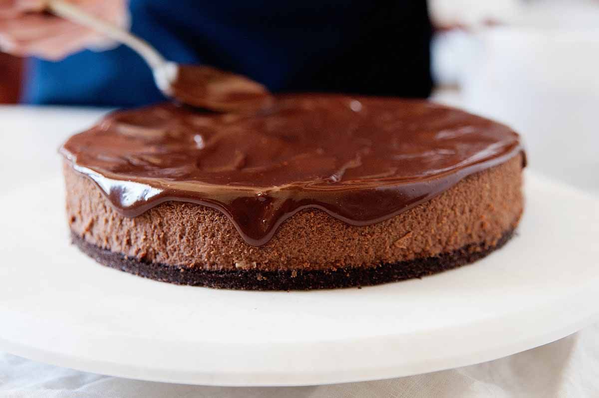 Using a spoon to smooth out the top of the ganache on chocolate cheesecake.
